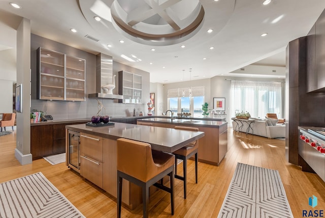 kitchen featuring a breakfast bar, a center island, wine cooler, wall chimney exhaust hood, and light hardwood / wood-style floors