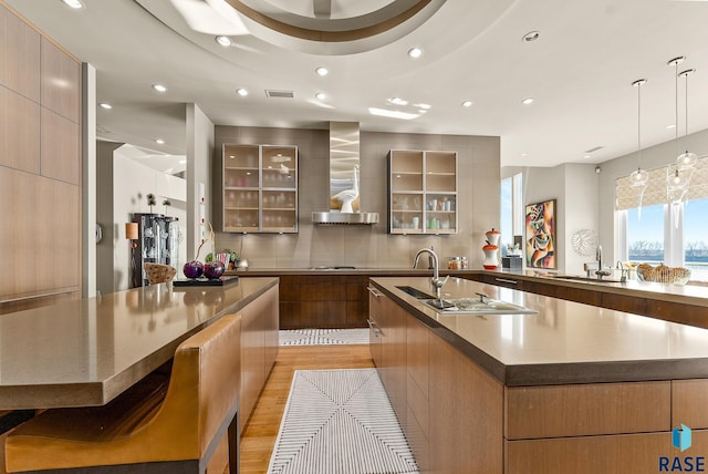 kitchen featuring wall chimney exhaust hood, sink, light hardwood / wood-style floors, hanging light fixtures, and a large island