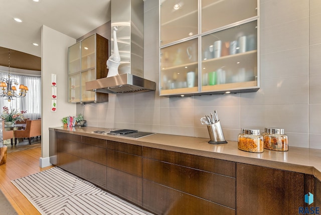 kitchen with tasteful backsplash, cooktop, wall chimney range hood, light hardwood / wood-style flooring, and a notable chandelier