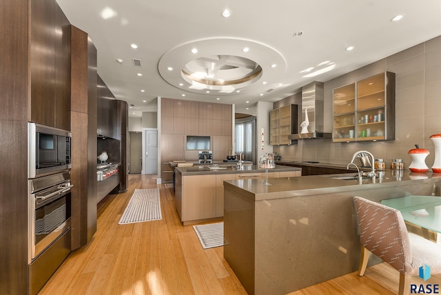 kitchen with built in microwave, a large island, sink, wall chimney range hood, and oven