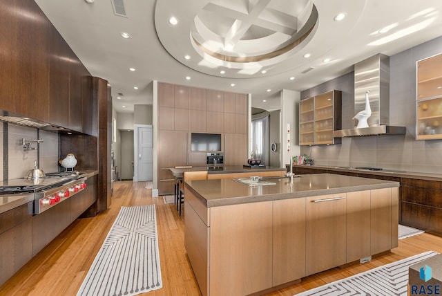 kitchen with coffered ceiling, a spacious island, electric stovetop, wall chimney range hood, and stainless steel gas stovetop