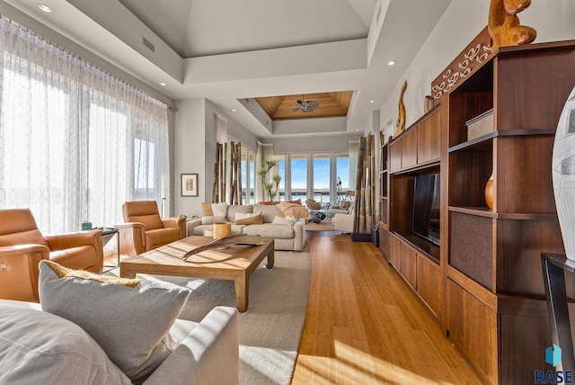 living room with a raised ceiling, ceiling fan, and light hardwood / wood-style flooring