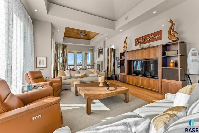 living room with a tray ceiling, ceiling fan, and light hardwood / wood-style floors