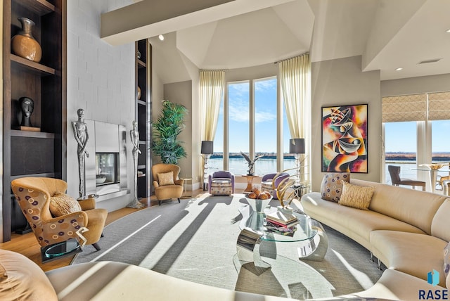 living room with built in features, hardwood / wood-style floors, a water view, and lofted ceiling