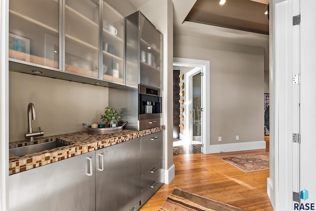 kitchen featuring stone counters, sink, stainless steel oven, a raised ceiling, and light hardwood / wood-style floors