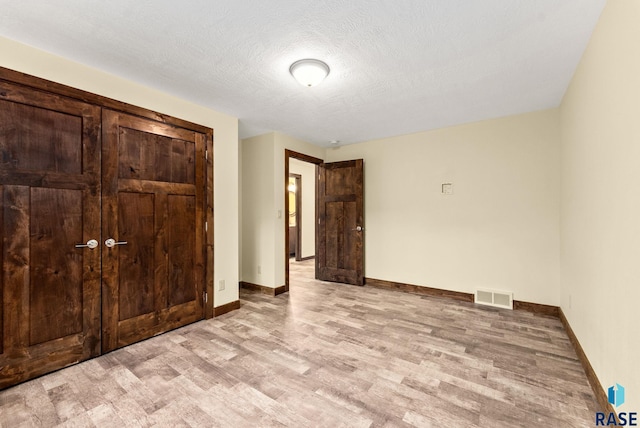 unfurnished bedroom with a textured ceiling, light hardwood / wood-style flooring, and a closet