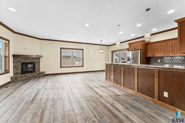 kitchen featuring a stone fireplace, stainless steel fridge, light stone countertops, light wood-type flooring, and decorative light fixtures