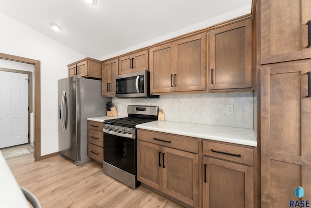 kitchen featuring appliances with stainless steel finishes, tasteful backsplash, vaulted ceiling, and light hardwood / wood-style floors