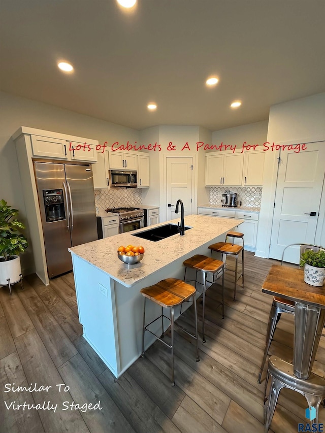 kitchen with sink, an island with sink, appliances with stainless steel finishes, a kitchen bar, and white cabinetry