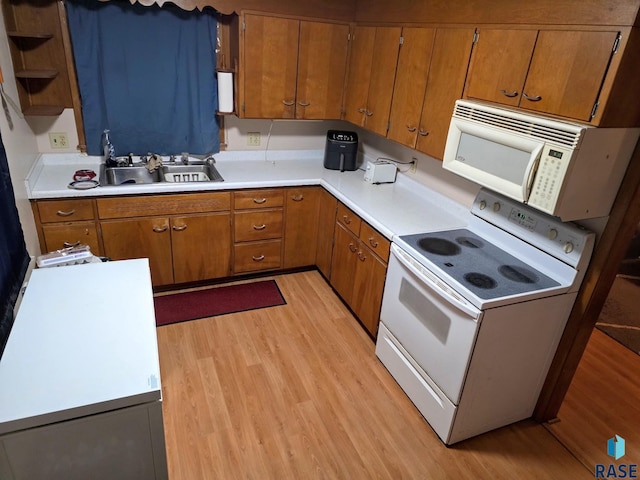 kitchen with white appliances, light wood-style flooring, brown cabinetry, and a sink