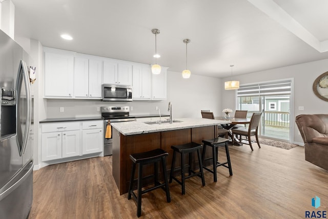 kitchen featuring hanging light fixtures, stainless steel appliances, an island with sink, sink, and white cabinetry