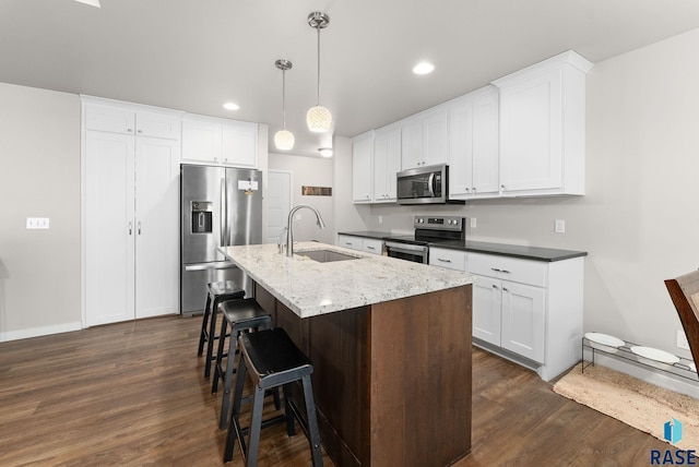 kitchen featuring a kitchen island with sink, hanging light fixtures, sink, appliances with stainless steel finishes, and white cabinets