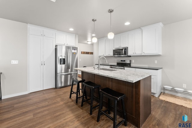 kitchen with sink, white cabinetry, decorative light fixtures, stainless steel appliances, and a kitchen island with sink