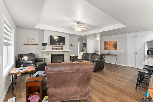 living room with a tray ceiling, ceiling fan, hardwood / wood-style floors, and a fireplace