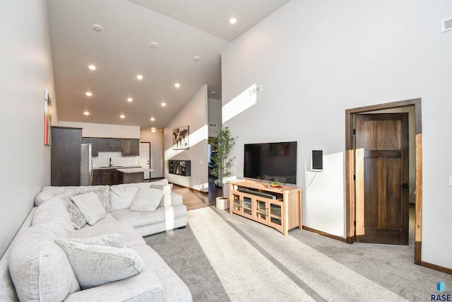 carpeted living room with sink and high vaulted ceiling