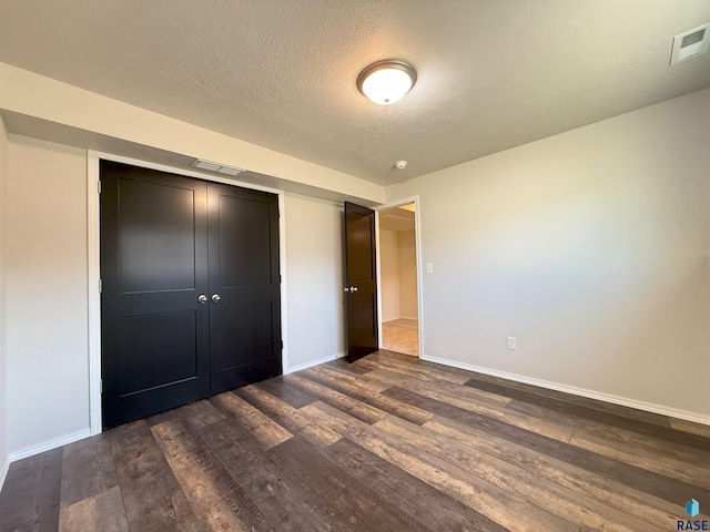 unfurnished bedroom with a textured ceiling, dark hardwood / wood-style flooring, and a closet