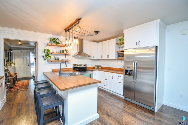 kitchen featuring wall chimney exhaust hood, stainless steel appliances, sink, a breakfast bar area, and butcher block counters