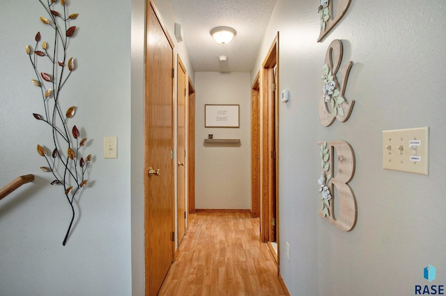 corridor with a textured ceiling and light wood-type flooring