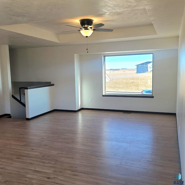 empty room featuring a raised ceiling, ceiling fan, and hardwood / wood-style floors