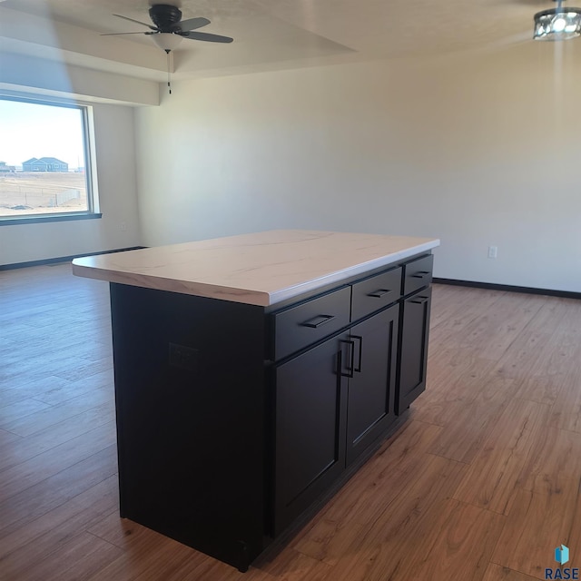 kitchen featuring light wood-type flooring, a center island, light stone counters, and ceiling fan