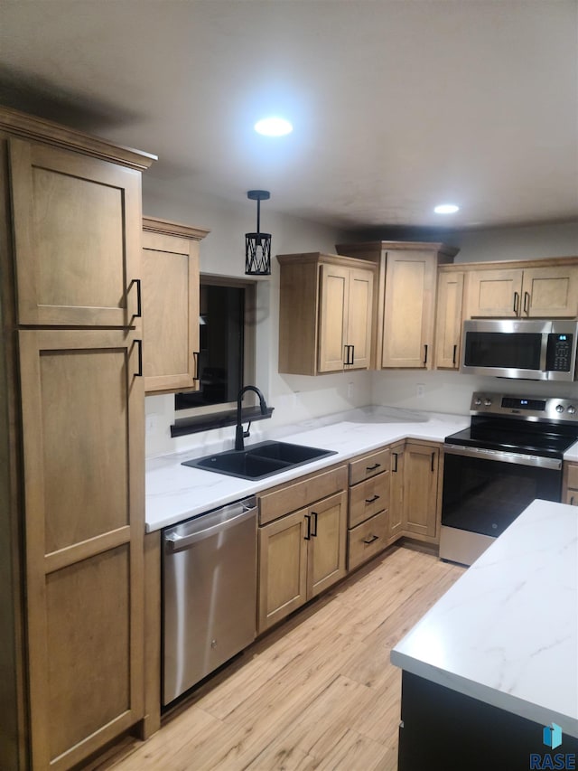 kitchen featuring sink, hanging light fixtures, stainless steel appliances, light stone counters, and light wood-type flooring