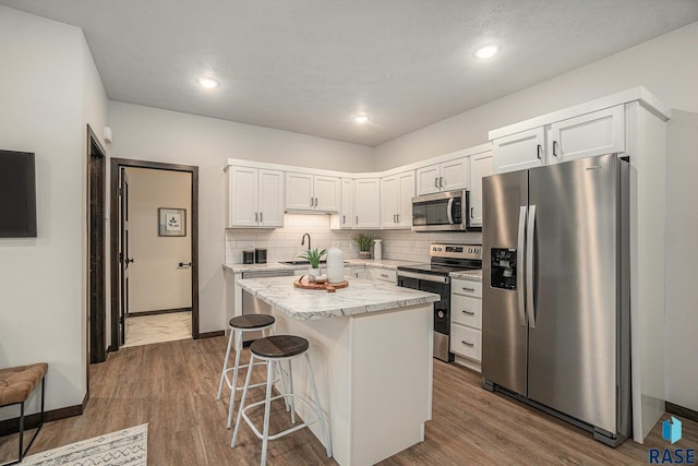 kitchen with sink, a breakfast bar area, a kitchen island, white cabinetry, and stainless steel appliances