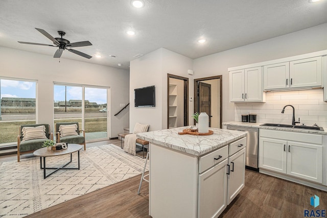 kitchen with dishwasher, sink, dark hardwood / wood-style floors, a kitchen island, and white cabinetry