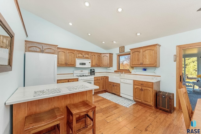 kitchen featuring white appliances, high vaulted ceiling, sink, light wood-type flooring, and a breakfast bar area