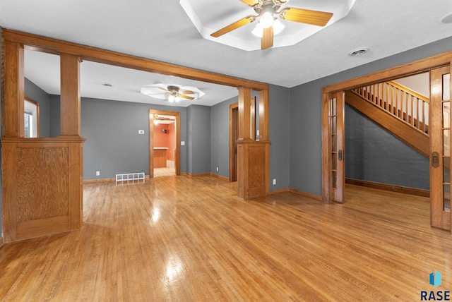 unfurnished living room featuring a raised ceiling, ceiling fan, and light hardwood / wood-style flooring