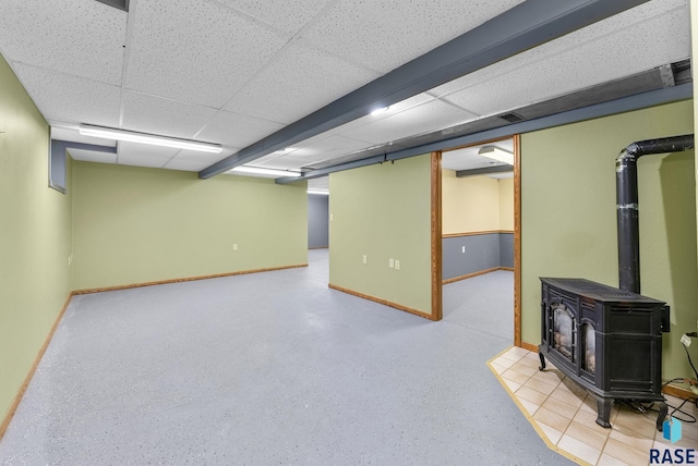 basement featuring a drop ceiling and a wood stove