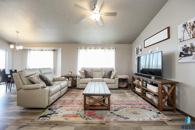 living room with vaulted ceiling, ceiling fan with notable chandelier, and hardwood / wood-style flooring