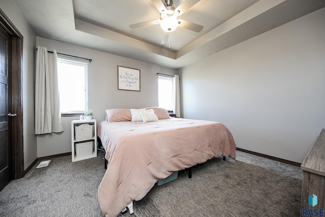 carpeted bedroom featuring multiple windows, ceiling fan, and a tray ceiling