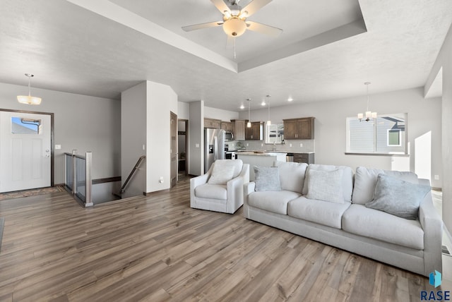 living room with hardwood / wood-style floors, ceiling fan with notable chandelier, and a raised ceiling