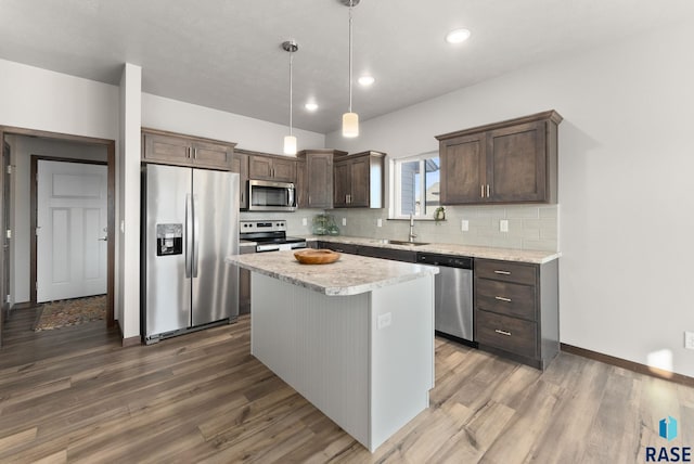 kitchen with sink, hanging light fixtures, stainless steel appliances, backsplash, and a kitchen island