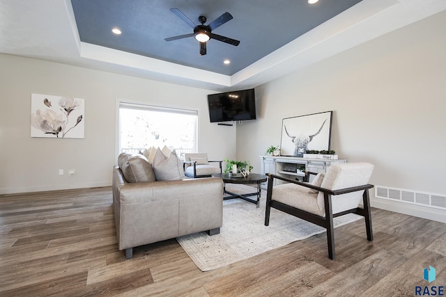 living room with a tray ceiling, ceiling fan, and wood-type flooring