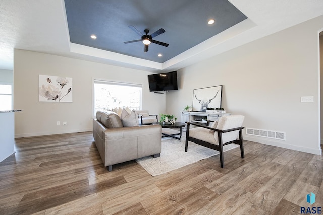 living room featuring light hardwood / wood-style flooring, a raised ceiling, and ceiling fan