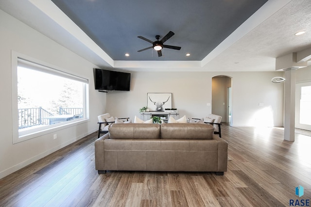 living room featuring ceiling fan, wood-type flooring, and a tray ceiling