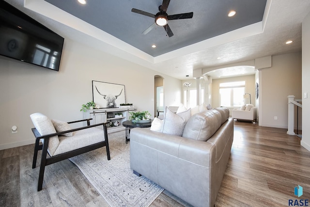 living room with a tray ceiling, ceiling fan, and wood-type flooring