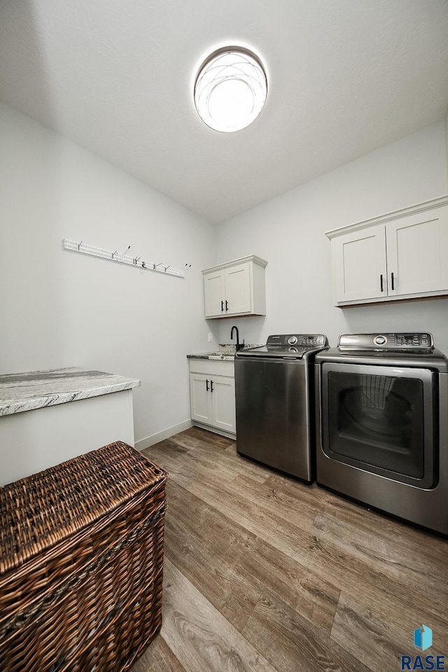 washroom with cabinets, light wood-type flooring, sink, and washing machine and clothes dryer