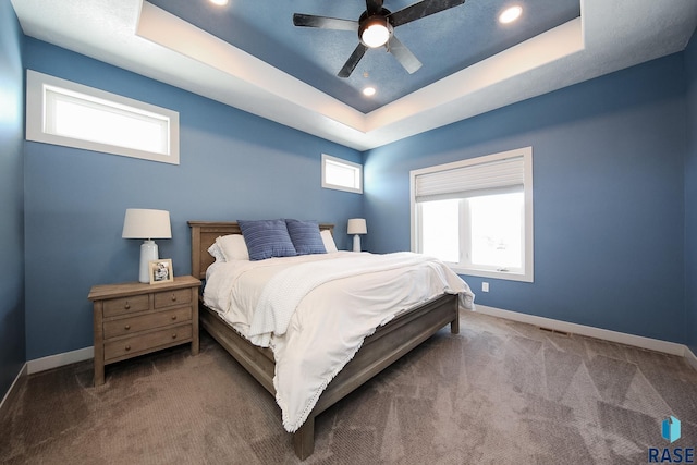 carpeted bedroom with a raised ceiling, multiple windows, and ceiling fan