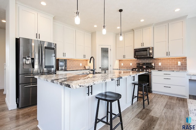 kitchen featuring decorative light fixtures, stainless steel appliances, white cabinetry, and an island with sink