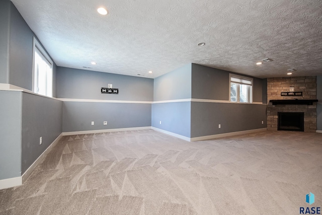 interior space featuring a stone fireplace, plenty of natural light, light colored carpet, and a textured ceiling