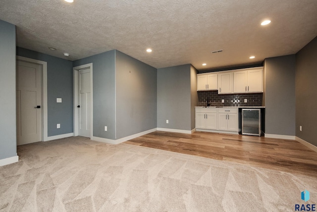 kitchen featuring light carpet, tasteful backsplash, a textured ceiling, beverage cooler, and white cabinetry