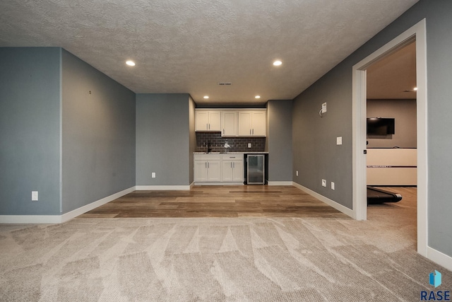 interior space featuring a textured ceiling, light colored carpet, sink, and beverage cooler