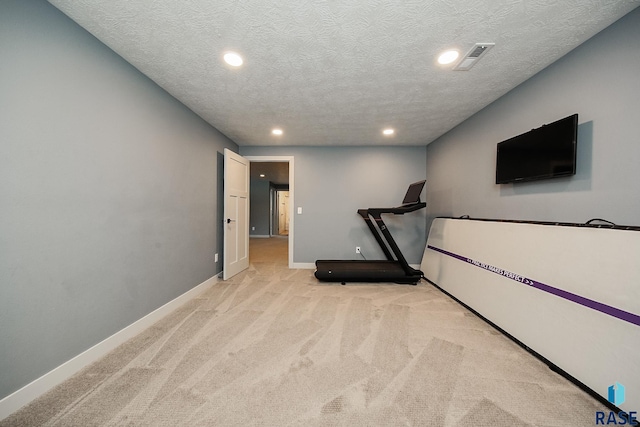 exercise room with light colored carpet and a textured ceiling