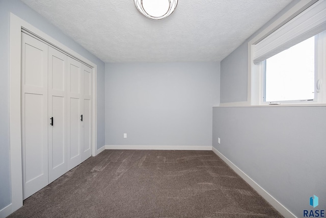 unfurnished bedroom with dark colored carpet, a textured ceiling, and a closet