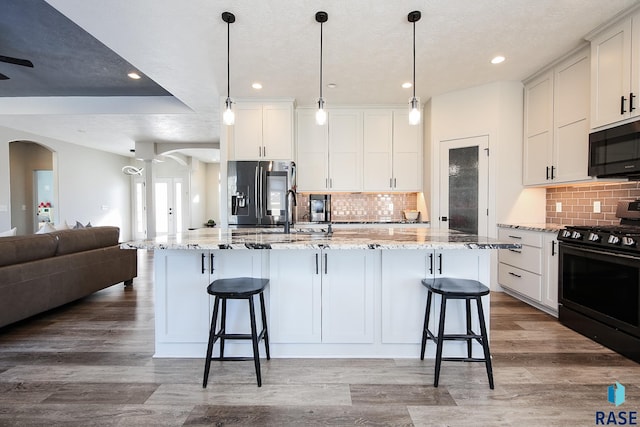 kitchen featuring black appliances, decorative light fixtures, light stone counters, and a kitchen island with sink