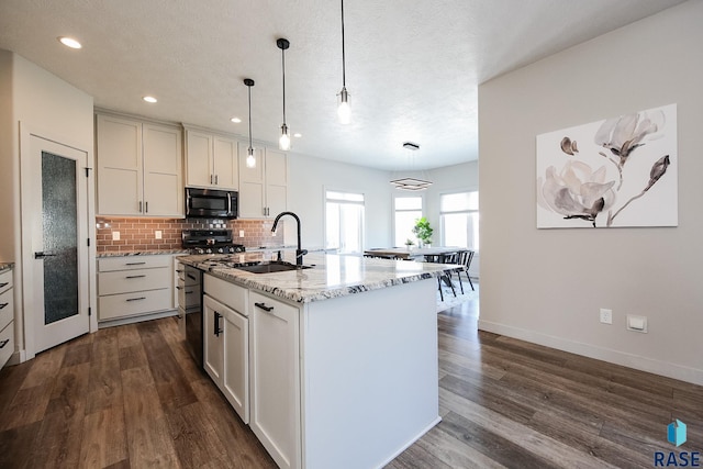 kitchen with a center island with sink, light stone countertops, sink, and hanging light fixtures