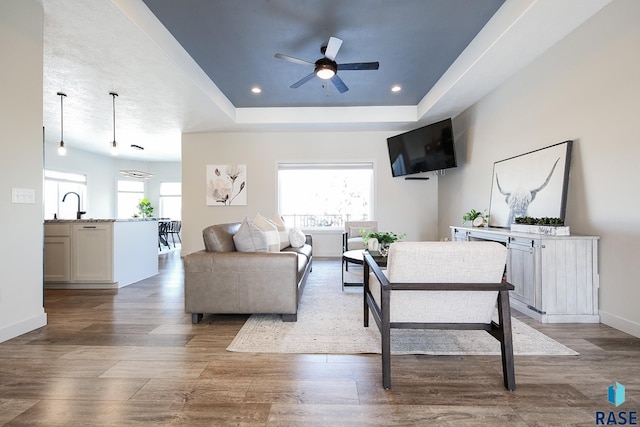 living room with a raised ceiling, ceiling fan, and sink