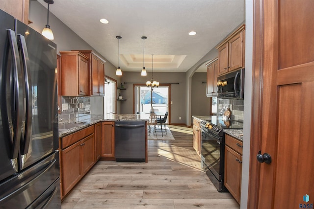 kitchen featuring a raised ceiling, kitchen peninsula, black appliances, and decorative light fixtures